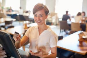 Woman in a coffee shop using a credit card to make a payment at a POS system, demonstrating modern payment processing.