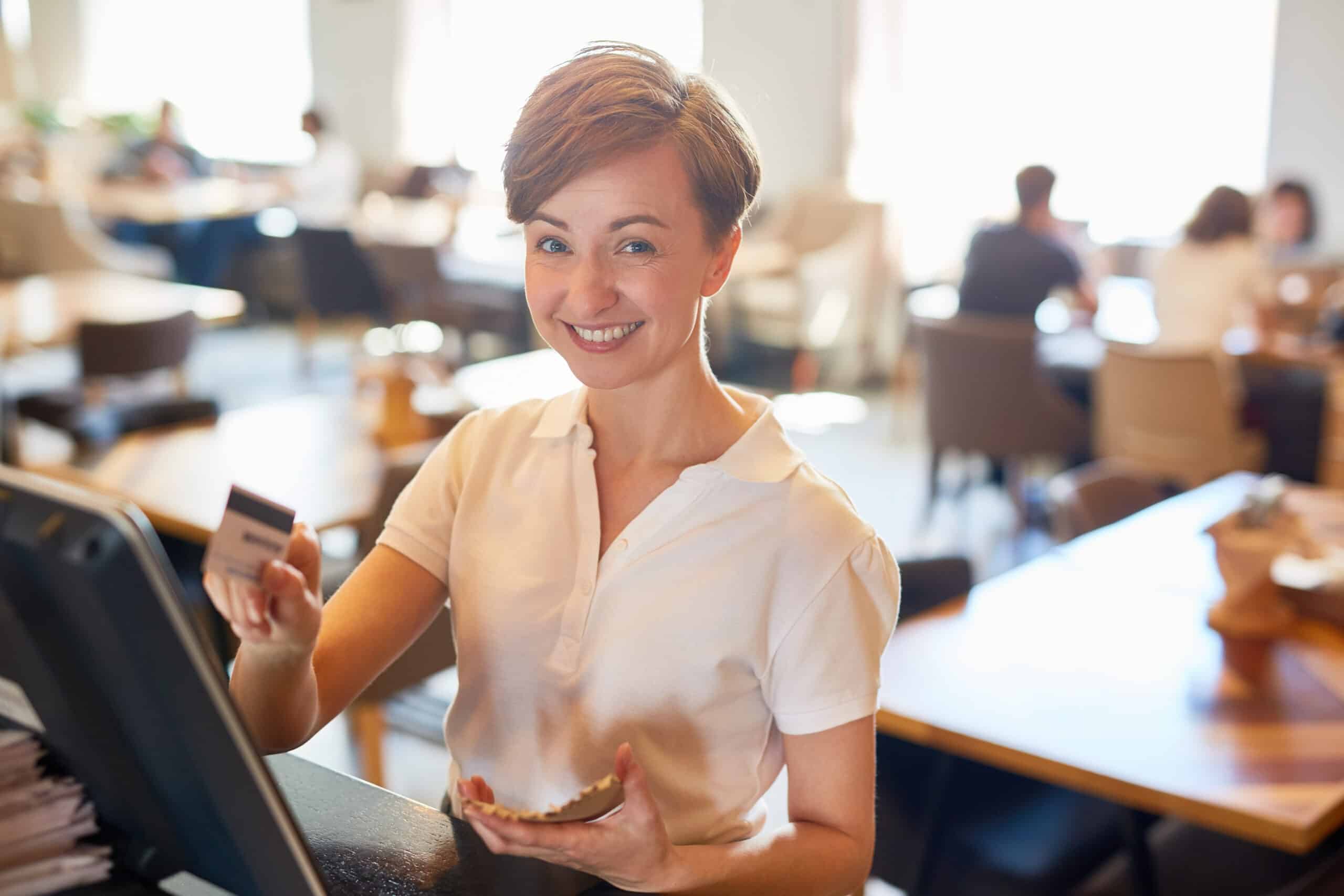 Woman in a coffee shop using a credit card to make a payment at a POS system, demonstrating modern payment processing.